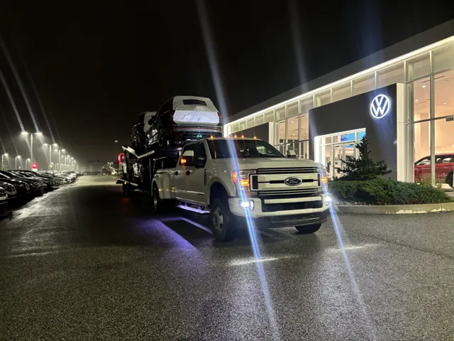 Loaded car hauler at a dealership lot at night